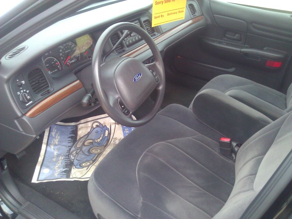 Interior shot of a Ford Crown Victoria, showing the dashboard, steering wheel, and seats. A yellow 'Sorry Sold To' sign is on the windshield