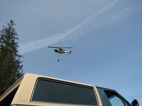 1990 Ford Bronco - A helicopter hovers in the sky with a person suspended beneath it, viewed from the perspective of someone looking up from a vehicle.