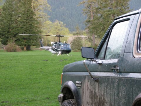 1990 Ford Bronco - A helicopter lands in a grassy field near a muddy green SUV.