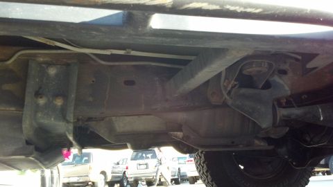 1996 Ford Bronco - The undercarriage of a vehicle shows its frame, suspension, and exhaust system with other vehicles in the background.