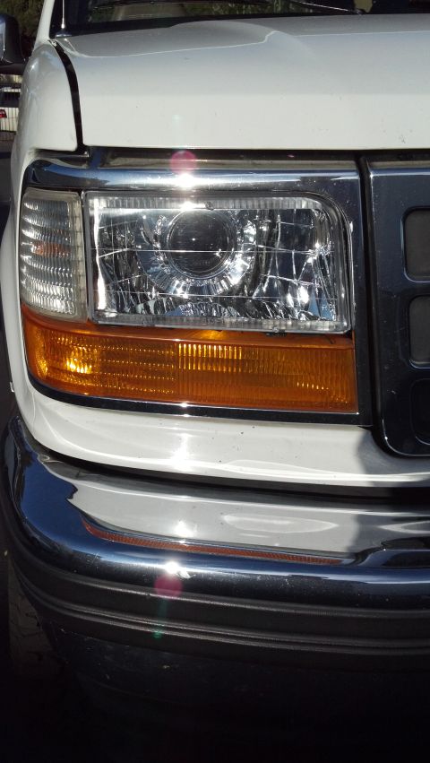 1996 Ford Bronco - Close-up of a white truck's front end, focusing on the headlight and grille assembly.