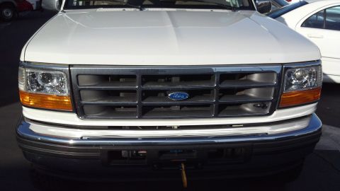 1996 Ford Bronco - This is a front view of a white Ford F-Series truck, showing its grille and headlights. Another vehicle is visible to the right.