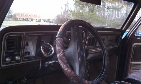 1979 Ford Bronco - The interior of a classic truck shows a wood-grain dashboard and a camouflage steering wheel cover.