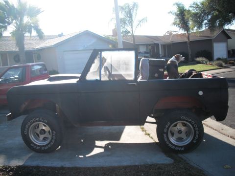 1968 Ford Bronco - Side view of a 1968 Ford Bronco in primer, with dogs in the back. Another vehicle is parked nearby.