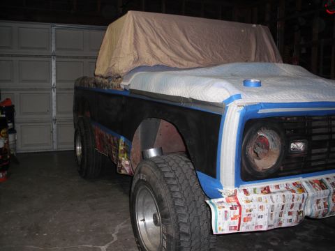 1968 Ford Bronco - Passenger-side 3/4 front view of a topless early Bronco in a home garage, masked off for paint with blue tape, a moving blanket over the ho…