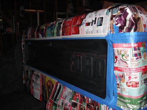 1968 Ford Bronco - The rear of a Ford truck masked off with newspaper ads and blue painter's tape, leaving only the tailgate exposed and freshly sprayed flat…