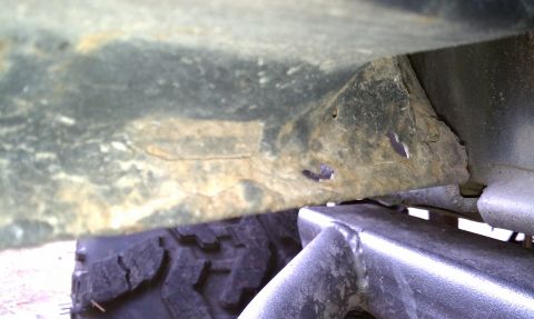 1979 Ford Bronco - Close-up view of a heavily rusted vehicle frame and a tire, supported by a jack.