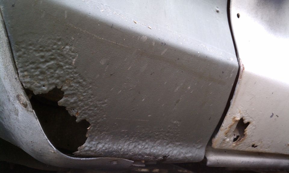 Rusted lower body panel with large hole