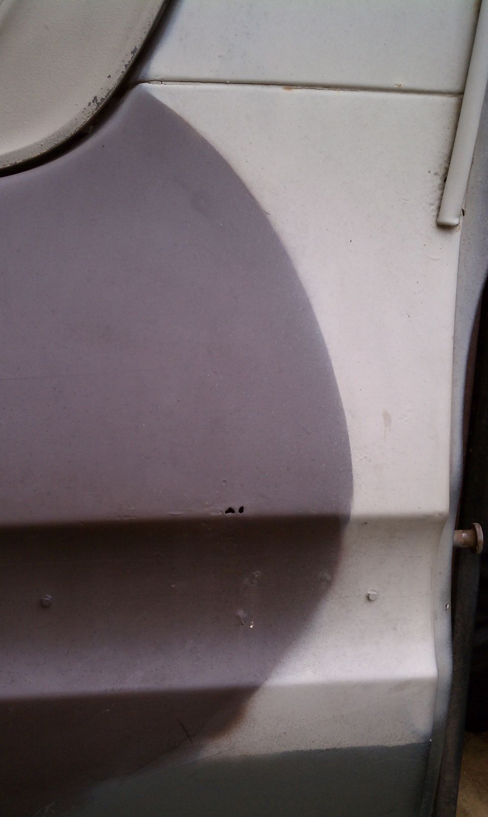 Close-up of a vehicle body panel with a two-tone camouflage paint scheme. Small rust spots are visible
