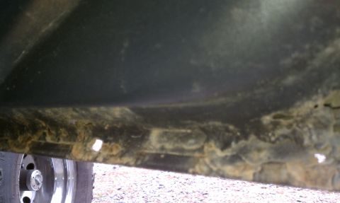 1979 Ford Bronco - Close-up view of a heavily rusted vehicle undercarriage, with a tire visible.