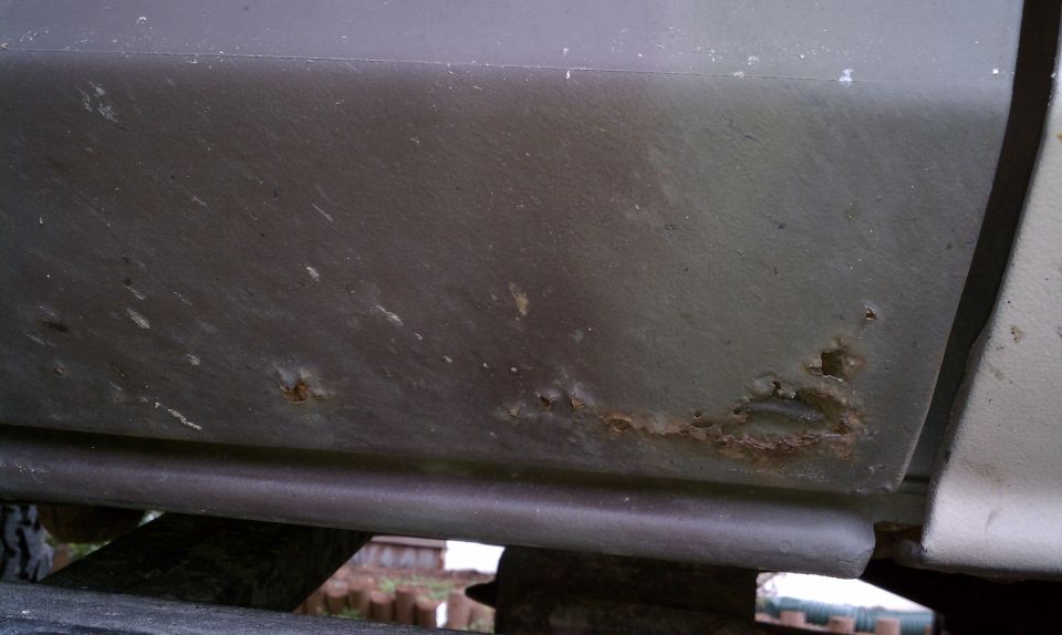 Close-up of rust on a vehicle's lower body panel, showing corrosion and damage
