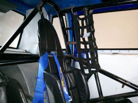 1967 Ford Mustang - Interior view of a race car, black racing seats and a blue safety harness, with a roll cage visible.