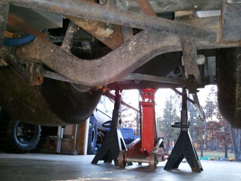 1967 Ford Mustang - The underside of a vehicle is supported by jack stands and a hydraulic jack, revealing its suspension and large tires.