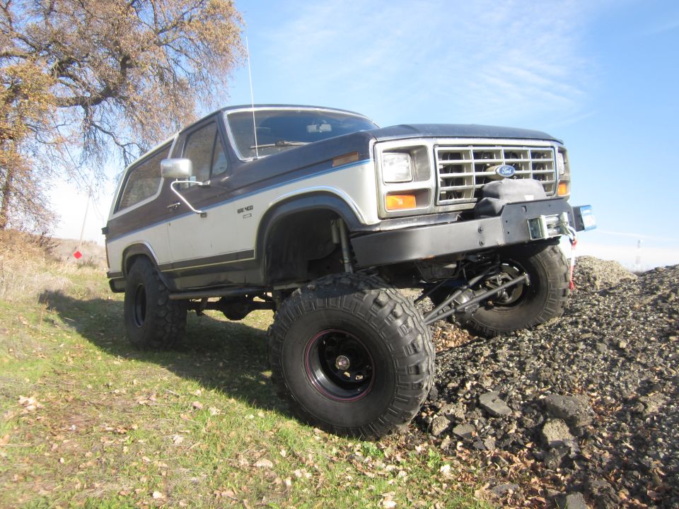 Lifted two-tone Ford Bronco with off-road tires on rocky terrain