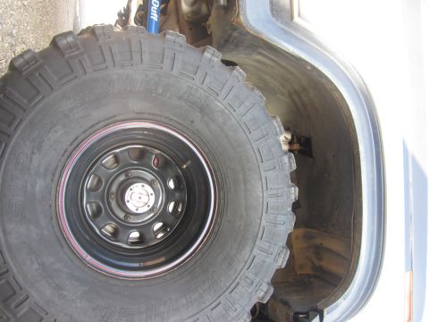 1985 Ford Bronco - A close-up view of a large off-road tire and the vehicle's wheel well, with a blue shock absorber partially visible.