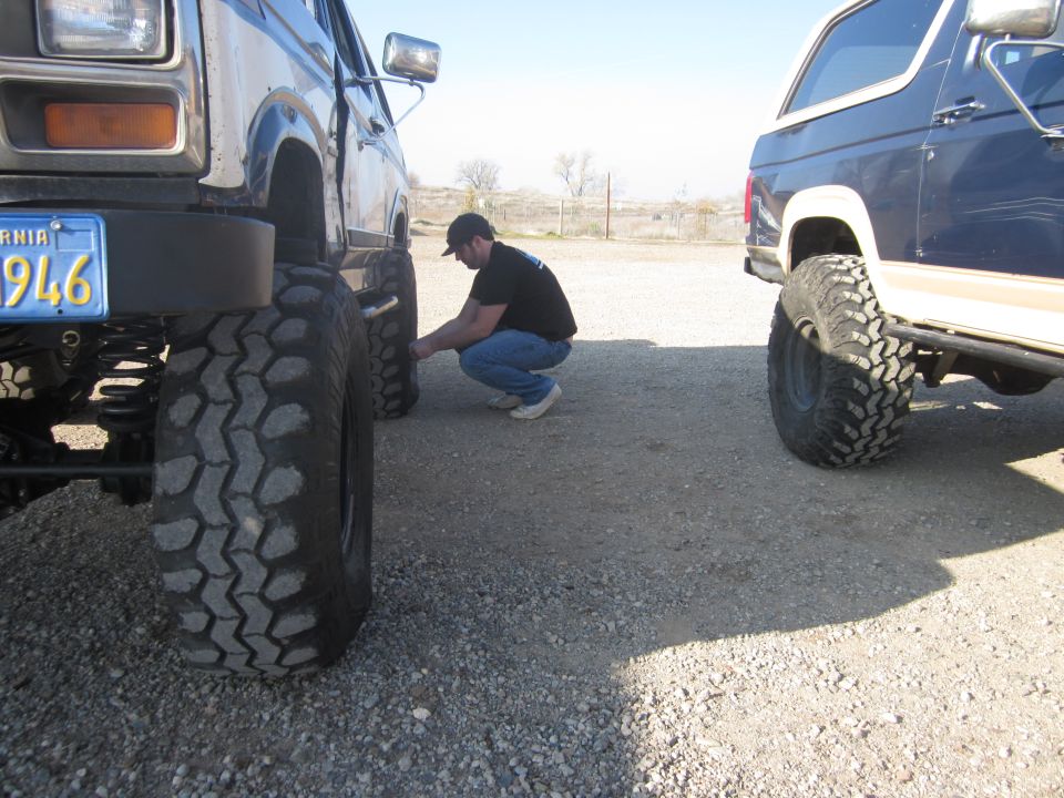 Man checking tire on lifted Ford Bronco next to another lifted Ford Bronco