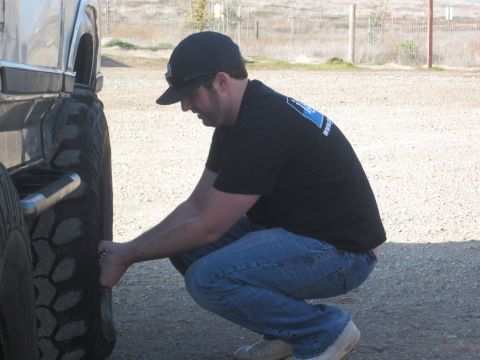 1985 Ford Bronco - A man inspects the tire of a large truck, possibly from the early 1980s.