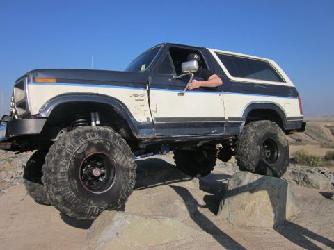 1985 Ford Bronco - This lifted Ford Bronco navigates a rocky trail under a clear blue sky.