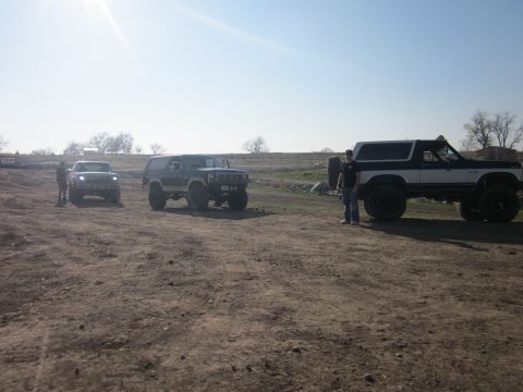 1985 Ford Bronco - Three modified SUVs are parked in an outdoor lot on a sunny day.