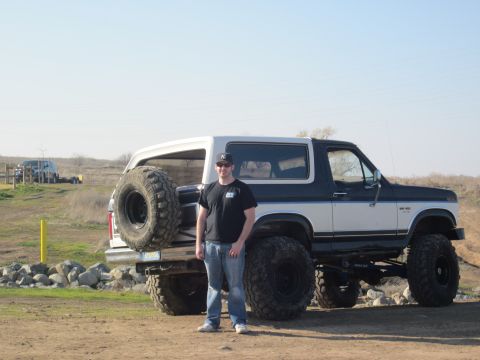 1985 Ford Bronco - A man poses with his modified Ford Bronco, oversized tires and a rear-mounted spare wheel.