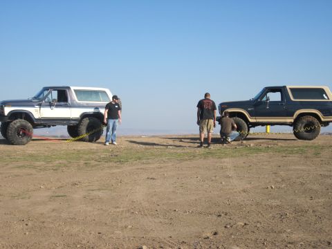 1985 Ford Bronco - Two Ford Broncos are shown in an outdoor setting, with individuals attending to their tires.