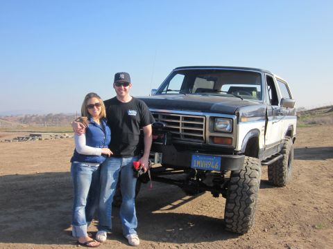 1985 Ford Bronco - Couple poses with a lifted 1980s Ford Bronco in an outdoor, dusty setting.
