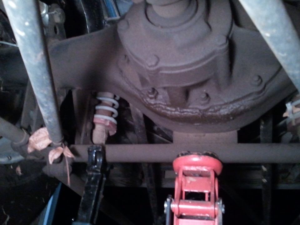 Rear axle housing and differential from below with suspension links and a red floor jack