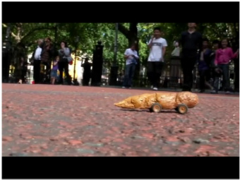 1969 Ford Torino - A novelty toy resembling dog feces, equipped with wheels, is positioned on a textured surface with a crowd of onlookers in the distance.