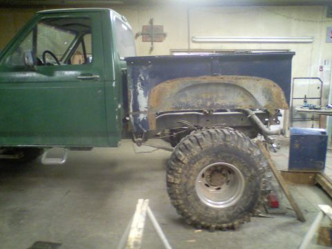 1989 Ford Bronco - This pickup truck is in a workshop, showing its side profile with the bed removed and a large tire.