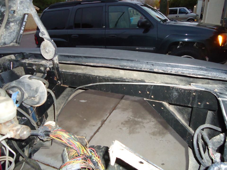 Close-up of a vehicle's engine bay with exposed wires. A dark SUV is parked behind it