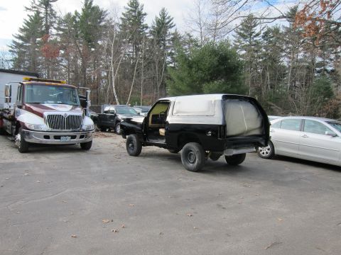 1987 Dodge 1500 - A black SUV, possibly undergoing bodywork, is parked next to a tow truck and a silver sedan.