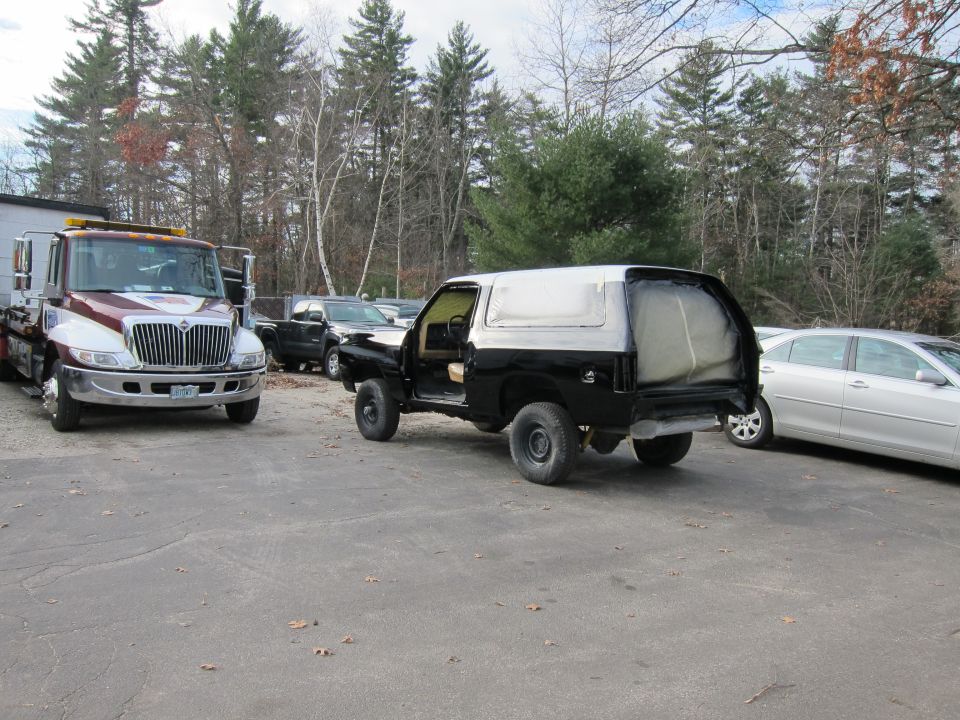 Black SUV in primer, rear view, with tow truck and sedan