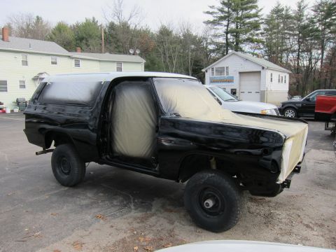 1987 Dodge 1500 - A black K5 Blazer is parked outside a garage, with its doors and hood covered in protective plastic sheeting.