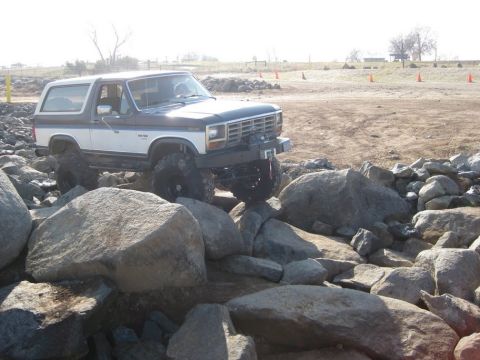 1985 Ford Bronco - This modified Ford Bronco is shown off-roading over a large rock obstacle.