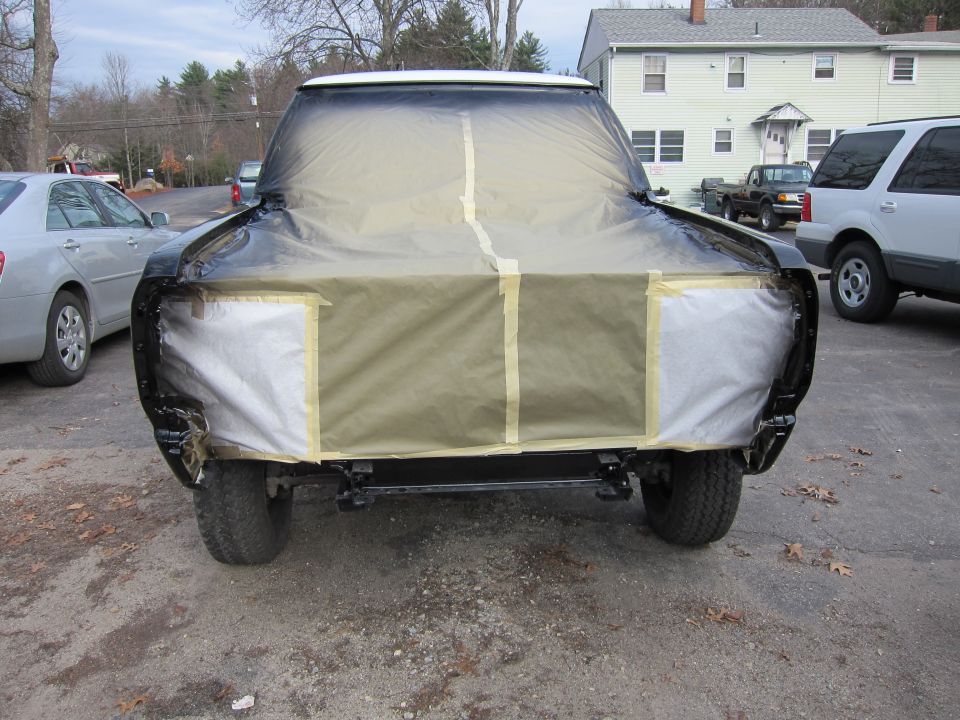 Front view of a truck covered in masking paper and tape, ready for paint. Other vehicles are parked nearby