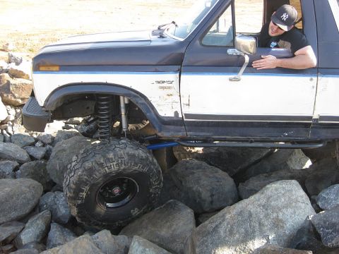 1985 Ford Bronco - A man drives a modified Ford Bronco over a rocky terrain.