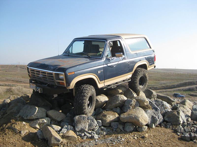 1985 Ford Bronco with lifted suspension and large tires climbing over a pile of rocks