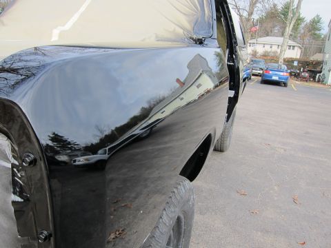1987 Dodge 1500 - Shiny black paint on a pickup truck's side panel, reflecting the surroundings. Other cars are visible in the parking lot.