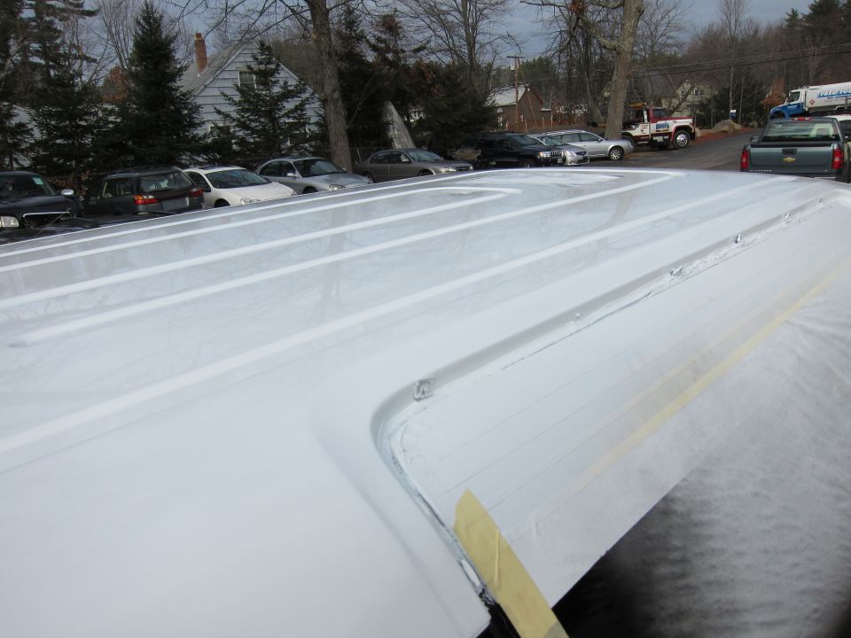 Close-up of a white pickup truck bed with ribbed sides, showing masking tape on the edge