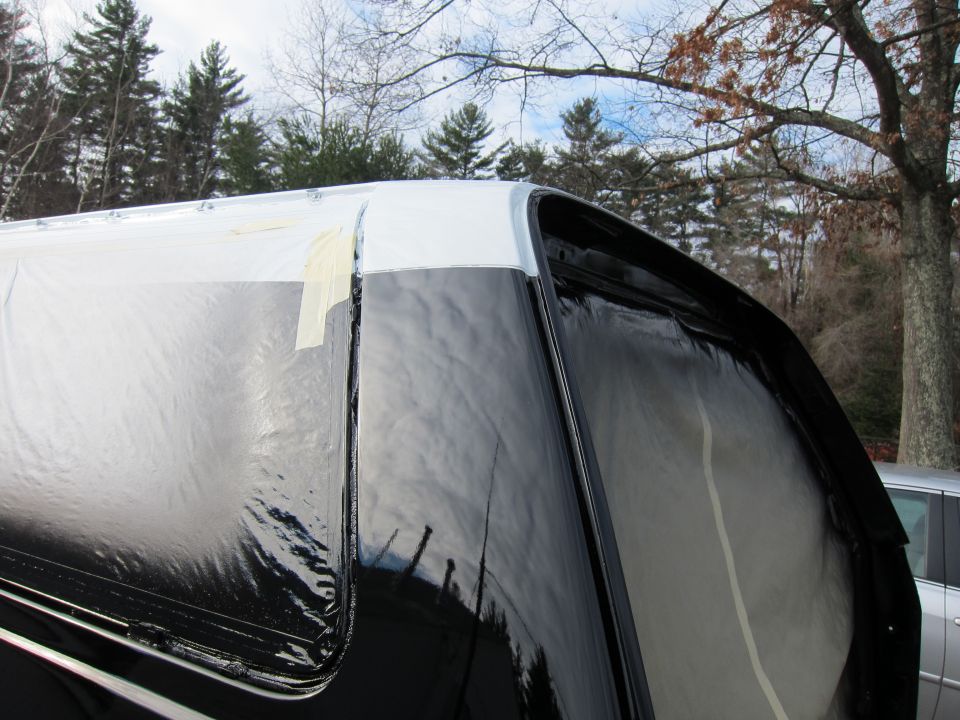 Top corner of a truck bed cap with black and white paint, covered in plastic and tape