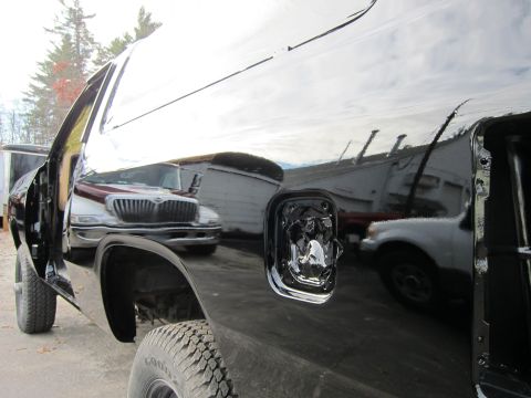 1987 Dodge 1500 - Reflection of a maroon and white International truck is visible on the glossy black side of a pickup truck.