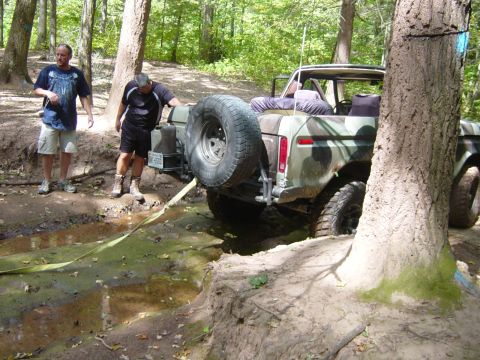 1979 Ford Bronco - A camouflaged Ford Bronco is stuck in a muddy trail with two men attempting to free it.
