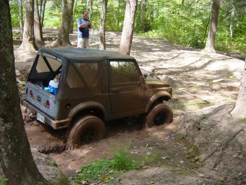 1979 Ford Bronco - An off-road vehicle navigates a challenging muddy terrain, with one wheel deep in the mire.