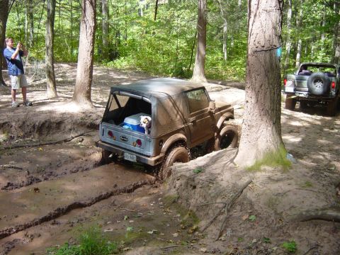 1979 Ford Bronco - Two off-road vehicles navigate a muddy trail in a wooded area.