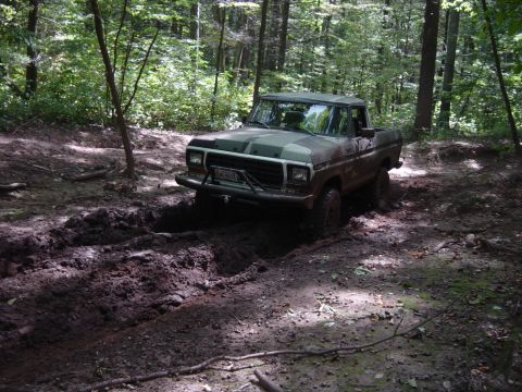 1979 Ford Bronco - A camouflaged Ford F-Series truck navigates a muddy trail in a wooded area.