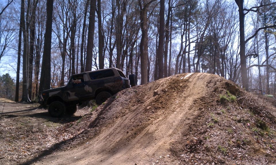 Off-road SUV climbing a dirt hill in a wooded area