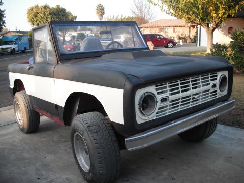 1968 Ford Bronco - Three-quarter front view of an early Ford Bronco roadster/half-cab in primer, wearing flat black upper body and hood over white lower panel…