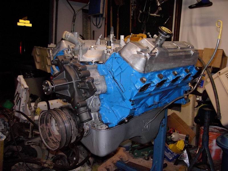 Blue-painted V8 engine with aluminum intake on a stand in a garage