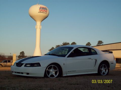 2000 Ford Mustang - A white 2000 Ford Mustang coupe is parked in front of a water tower and a building.