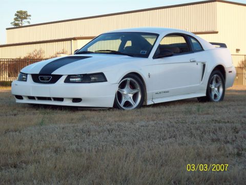 2000 Ford Mustang - A white 2000 Ford Mustang with racing stripes is parked outside a building.